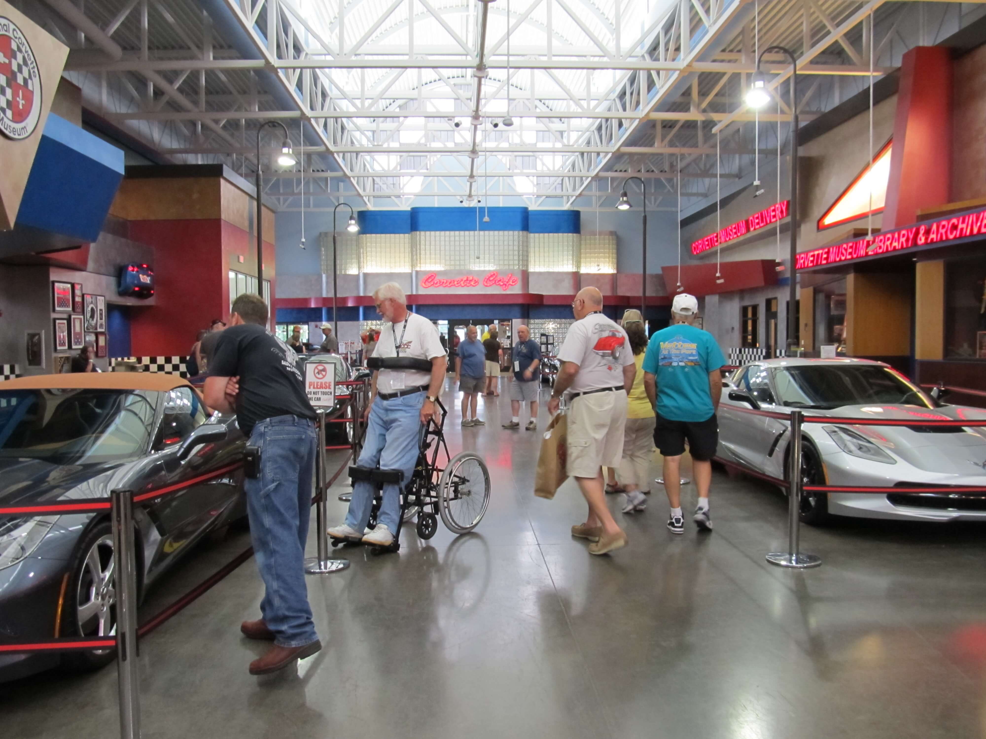 Photo of Simon in a standing wheelchair looking at new Corvettes at the National Corvette Museum